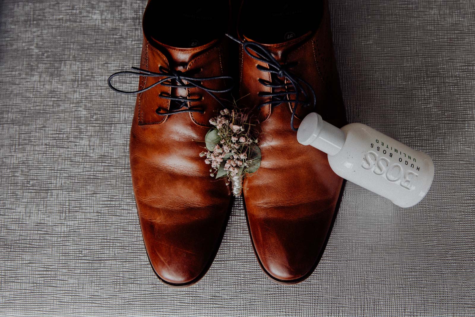 Schuhe des Braeutigams beim Getting Ready mit PArfum und Blumen arrangiert